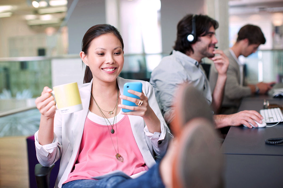 Girl in office scrolling through smart phone, smiling