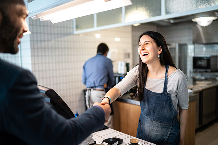 Two adults shaking hands over a coffee shop counter