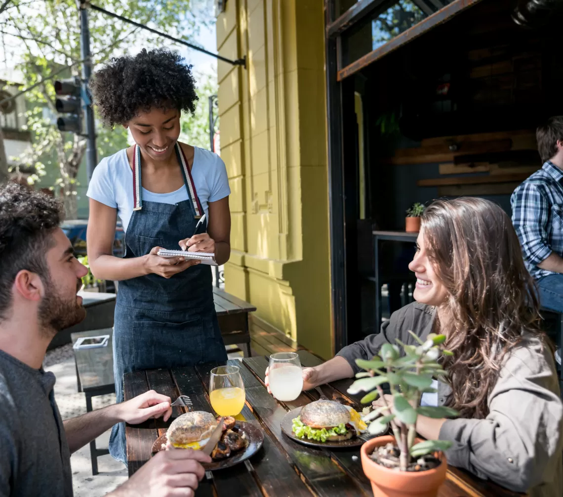 Waitress taking the order of two people sitting outdoors at a restaurant 