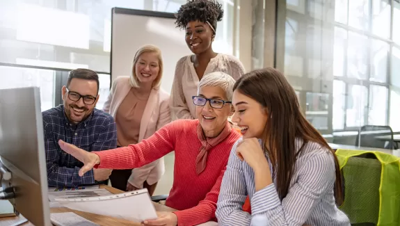 A diverse group of people gathered around a computer. 