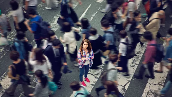 One person in focus, looking at the camera, in a busy cross walk, many other people walking by out of focus