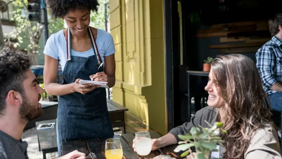 Waitress taking the order of two people sitting outdoors at a restaurant 